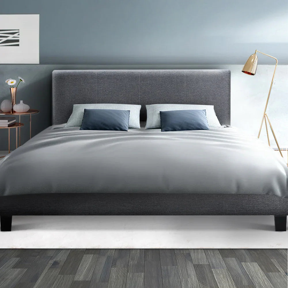 Modern gray upholstered bed with blue pillows, gray bedding, wooden floor, blue wall, and gold floor lamp