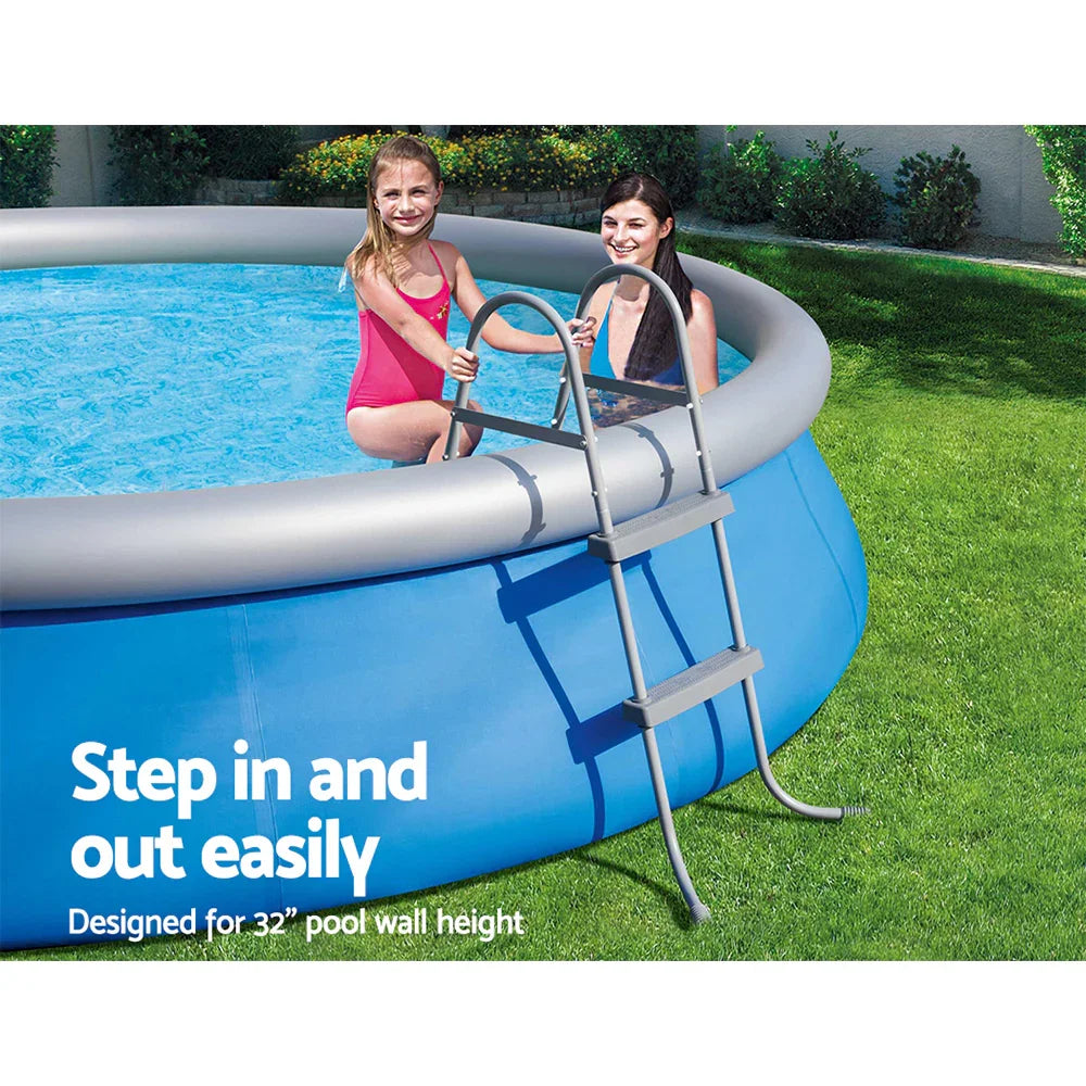 Two girls in an above ground blue pool using a gray ladder on green grass
