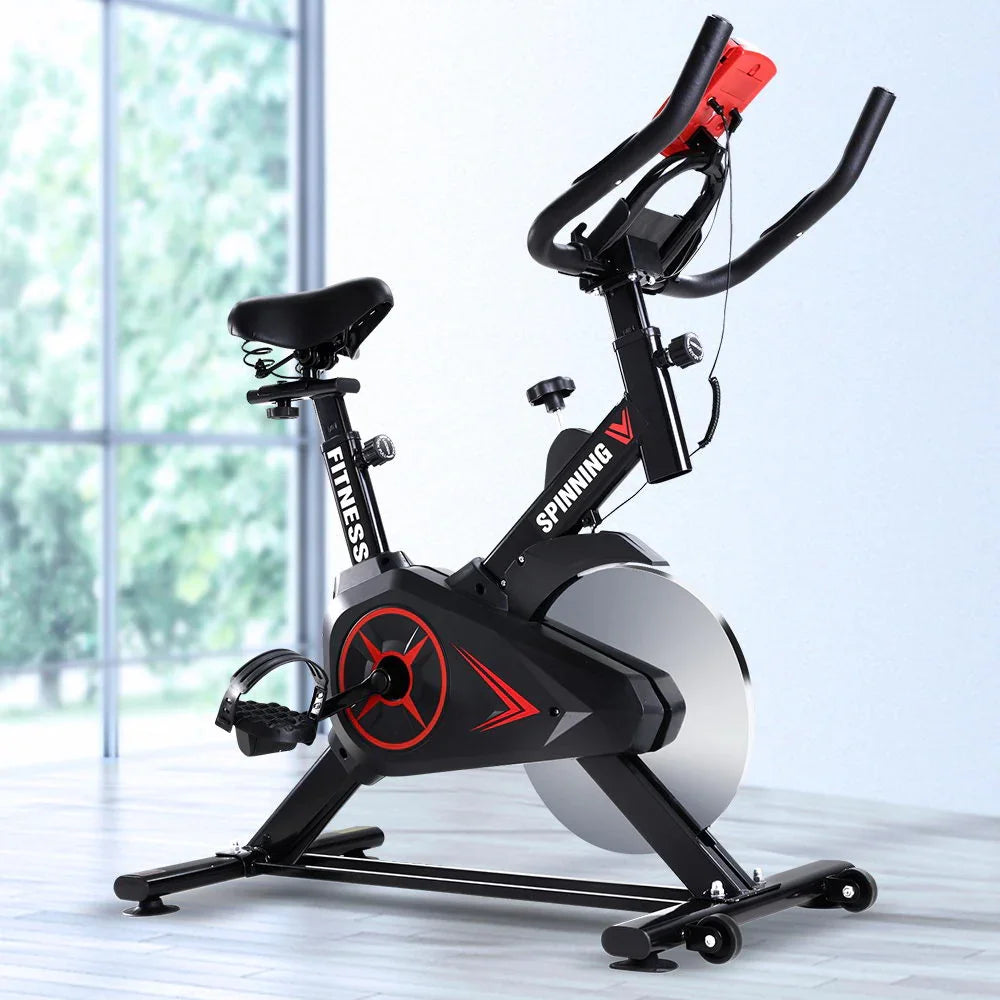 Black indoor exercise spinning bike with red accents in a bright room