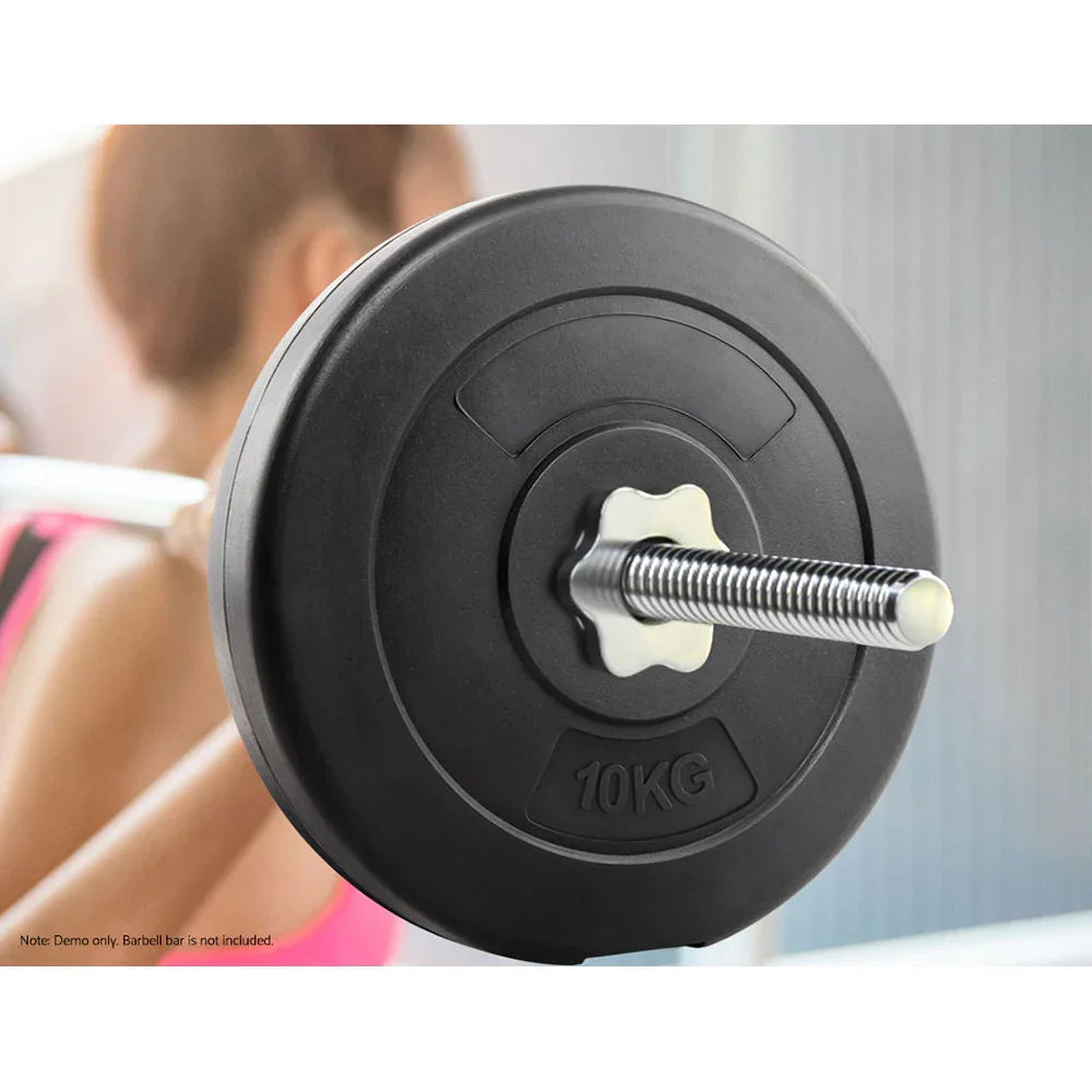 Close-up of 10kg black weight plate on barbell with blurred woman in pink workout attire