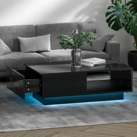 Modern black coffee table with LED lighting, glass vase, books, in a gray living room.
