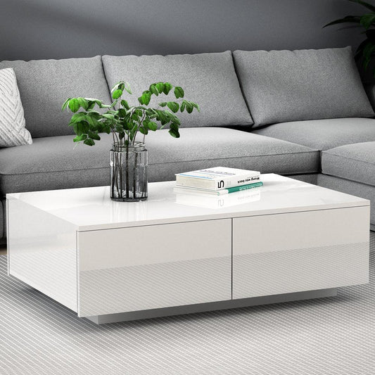 Modern white gloss coffee table with plant and books, in front of a grey sectional sofa