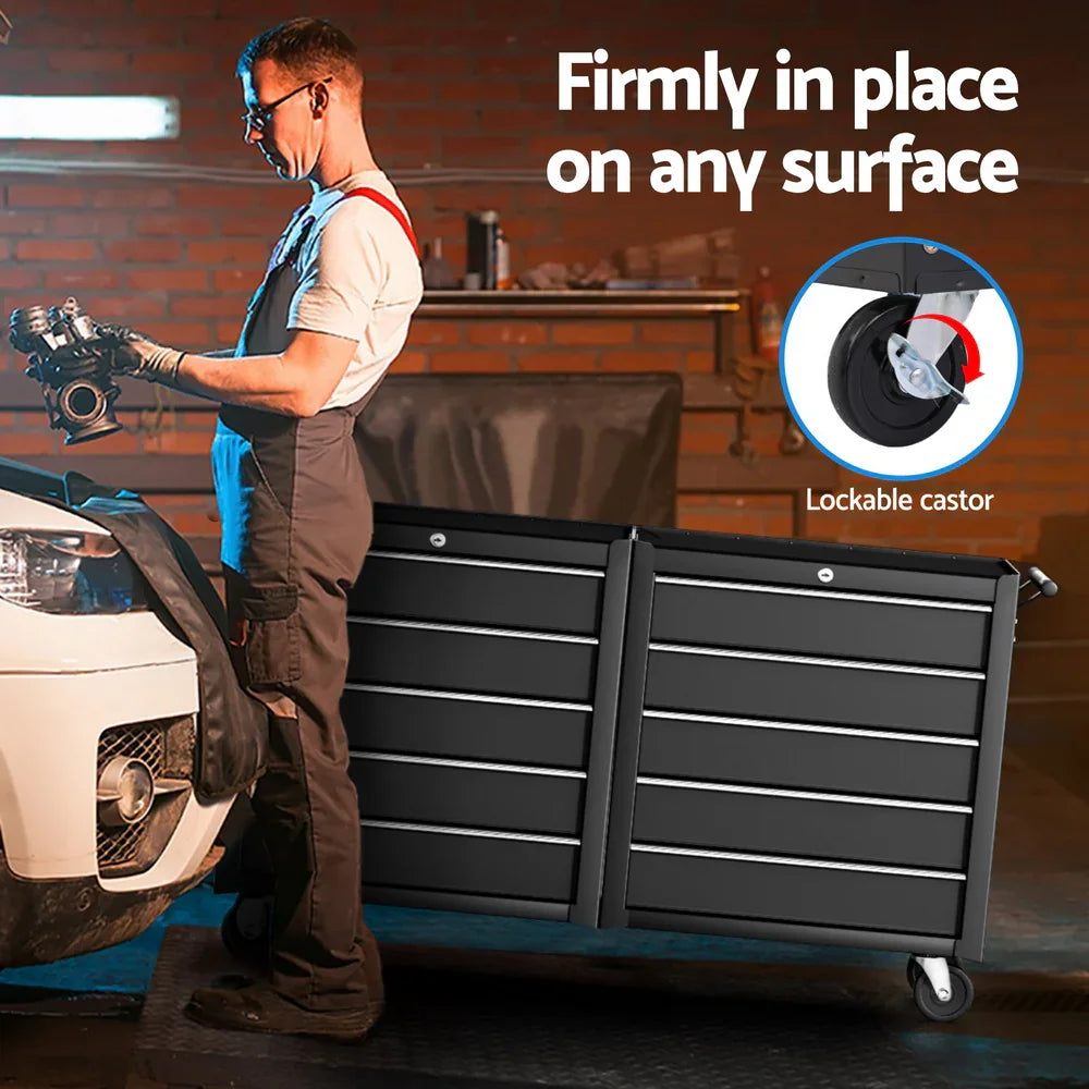 Mechanic holding engine part beside large black tool chest with lockable castor wheel in garage