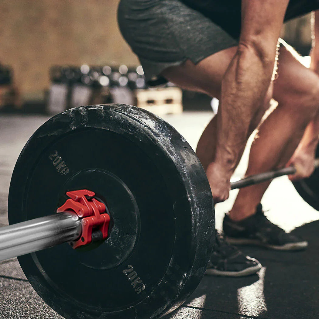 Man in gym shorts deadlifting barbell with 20kg weights on gym floor
