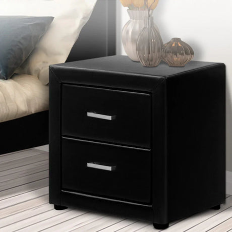 Black leather nightstand with two drawers beside a bed, vases on top, modern bedroom