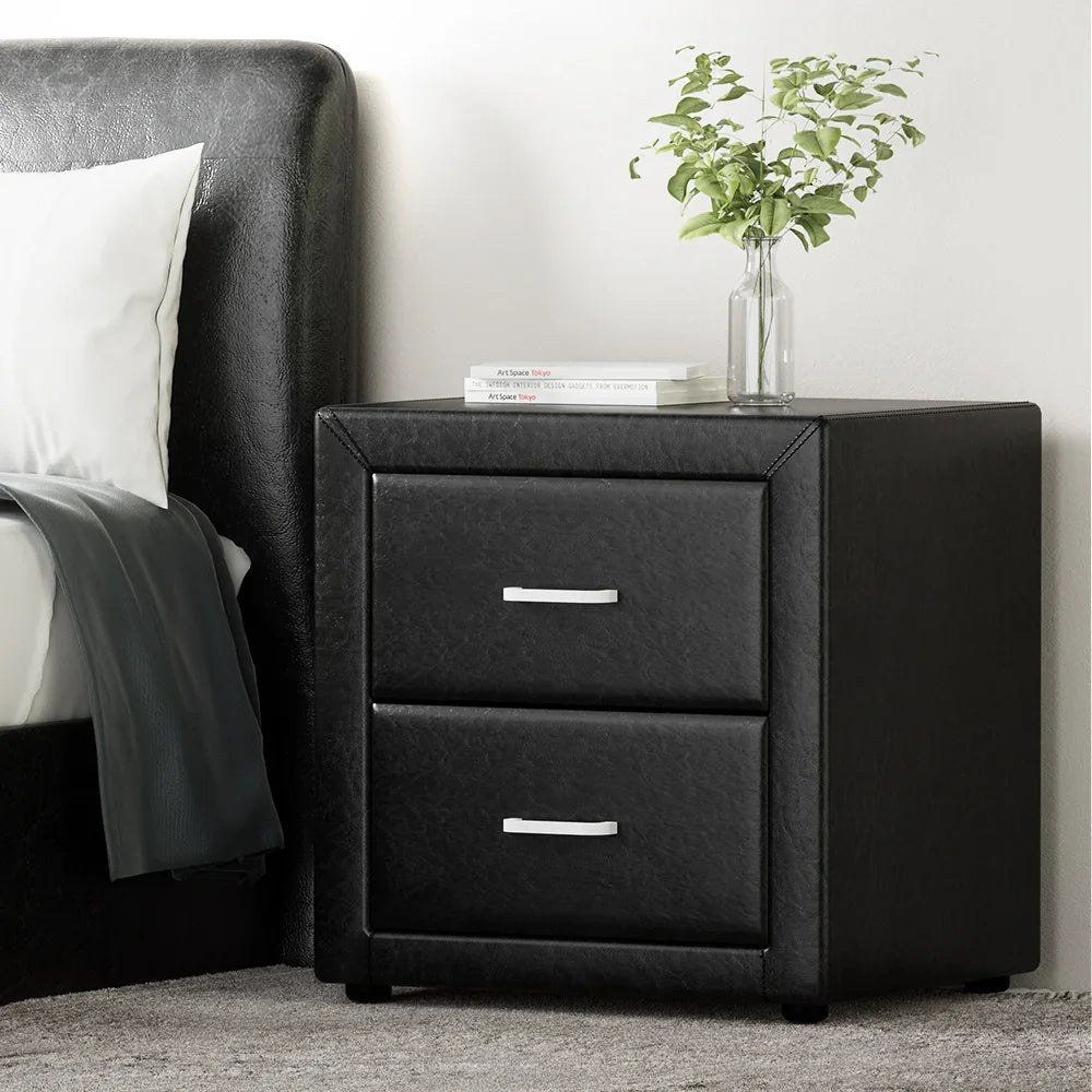 Modern black leather nightstand with two drawers beside a bed, vase and books on top