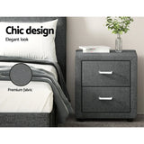 Modern gray fabric bedside table with two drawers beside upholstered bed, books, and vase
