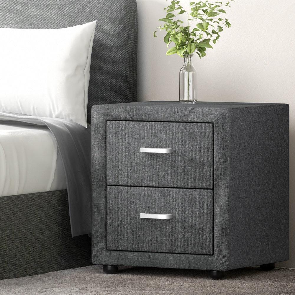 Modern gray fabric nightstand with two drawers beside a bed, glass vase with green plant on top