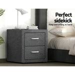 Modern gray fabric nightstand with two drawers beside a bed, lamp, and books on top