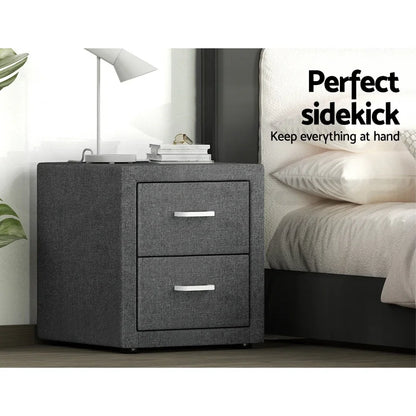 Modern gray fabric nightstand with two drawers beside a bed, lamp, and books on top