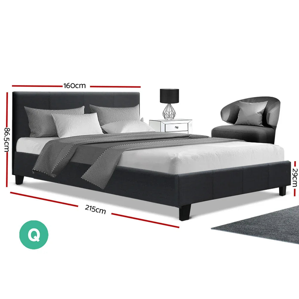 Modern queen size black upholstered bed with gray bedding, pillows, side table, lamp, and gray armchair