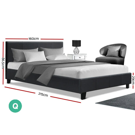 Modern queen size black upholstered bed with gray bedding, pillows, side table, lamp, and gray armchair