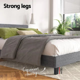 Modern grey upholstered bed with 13cm legs, green pillows, gray blanket, and indoor plants near window