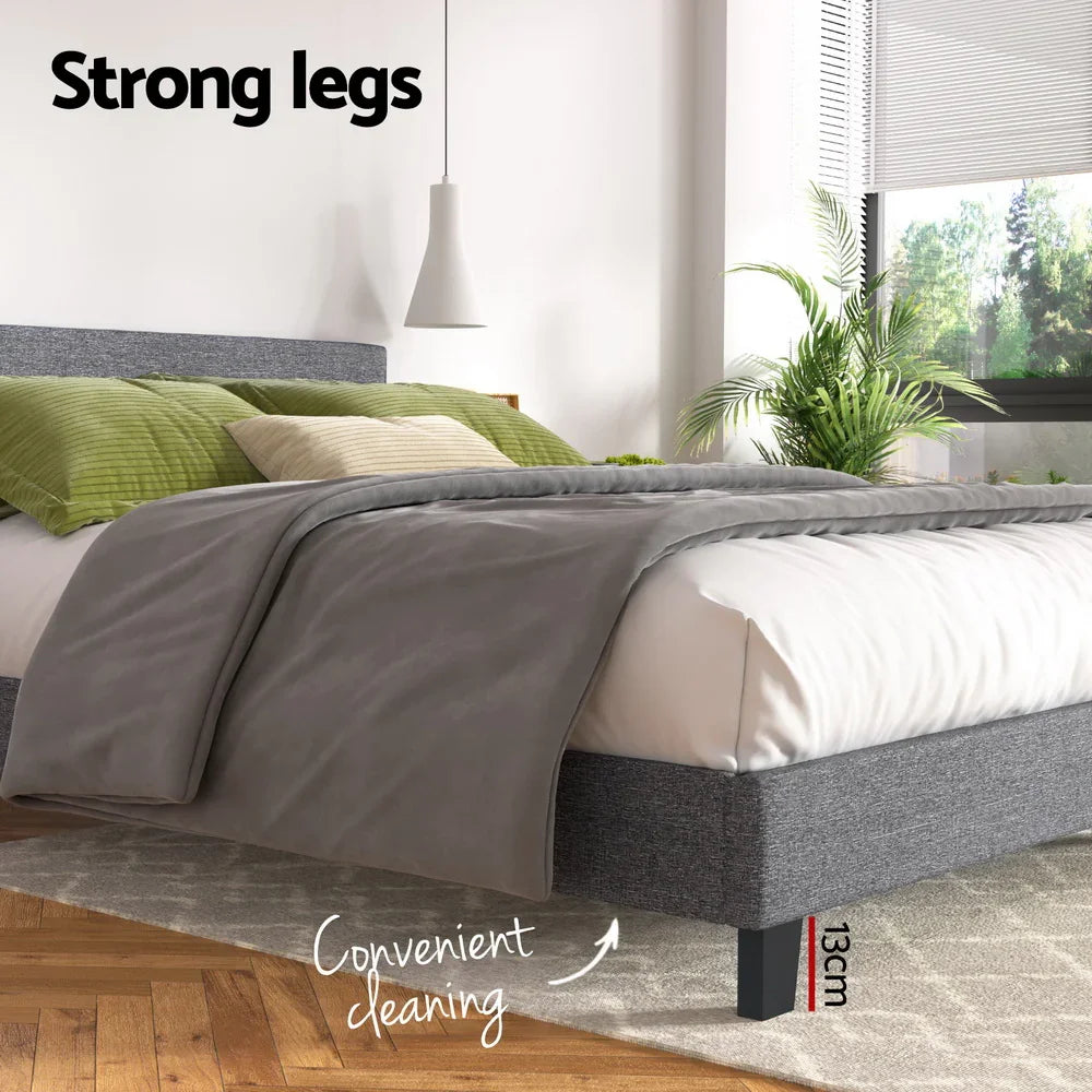 Modern grey upholstered bed with 13cm legs, green pillows, gray blanket, and indoor plants near window