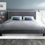 Modern gray upholstered bed with blue pillows, gray bedding, wooden floor, blue wall, and gold floor lamp