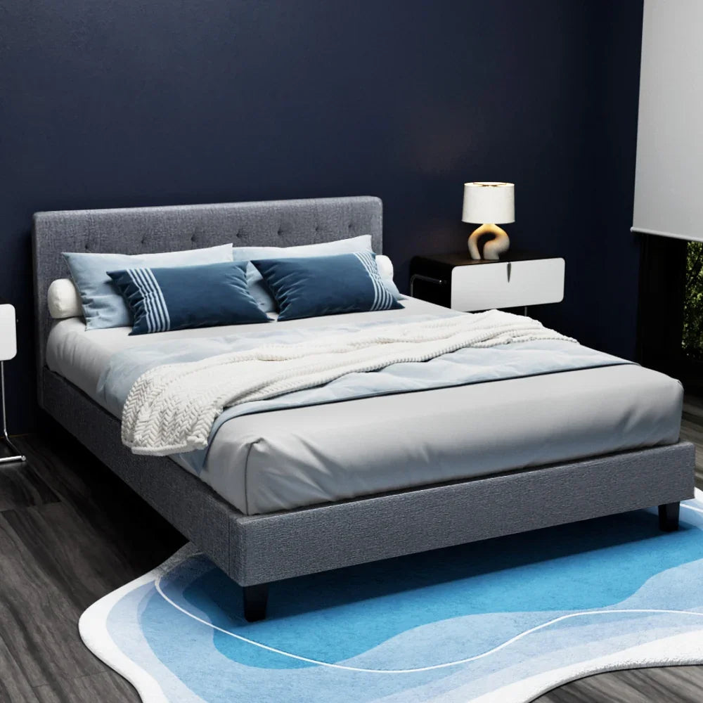 Modern bedroom with gray upholstered bed, blue and white bedding, decorative pillows, abstract blue rug, bedside table with lamp