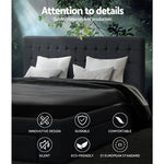 Dark gray upholstered bed with white pillows and black bedding under green leafy branches with quality and design icons