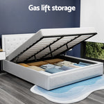 White upholstered bed with gas lift storage open showing neatly folded blankets inside, modern bedroom with blue wall and window view