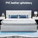 Modern white PVC leather upholstered bed with blue pillows, white nightstands, and lamp on blue rug