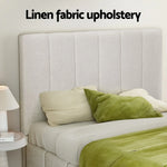 Bed with linen fabric upholstered headboard, green pillows, green blanket, and bedside table with lamp