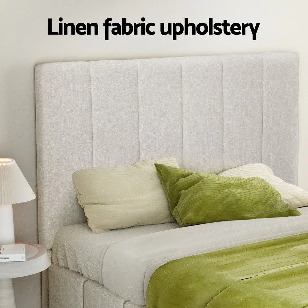 Bed with linen fabric upholstered headboard, green pillows, green blanket, and bedside table with lamp