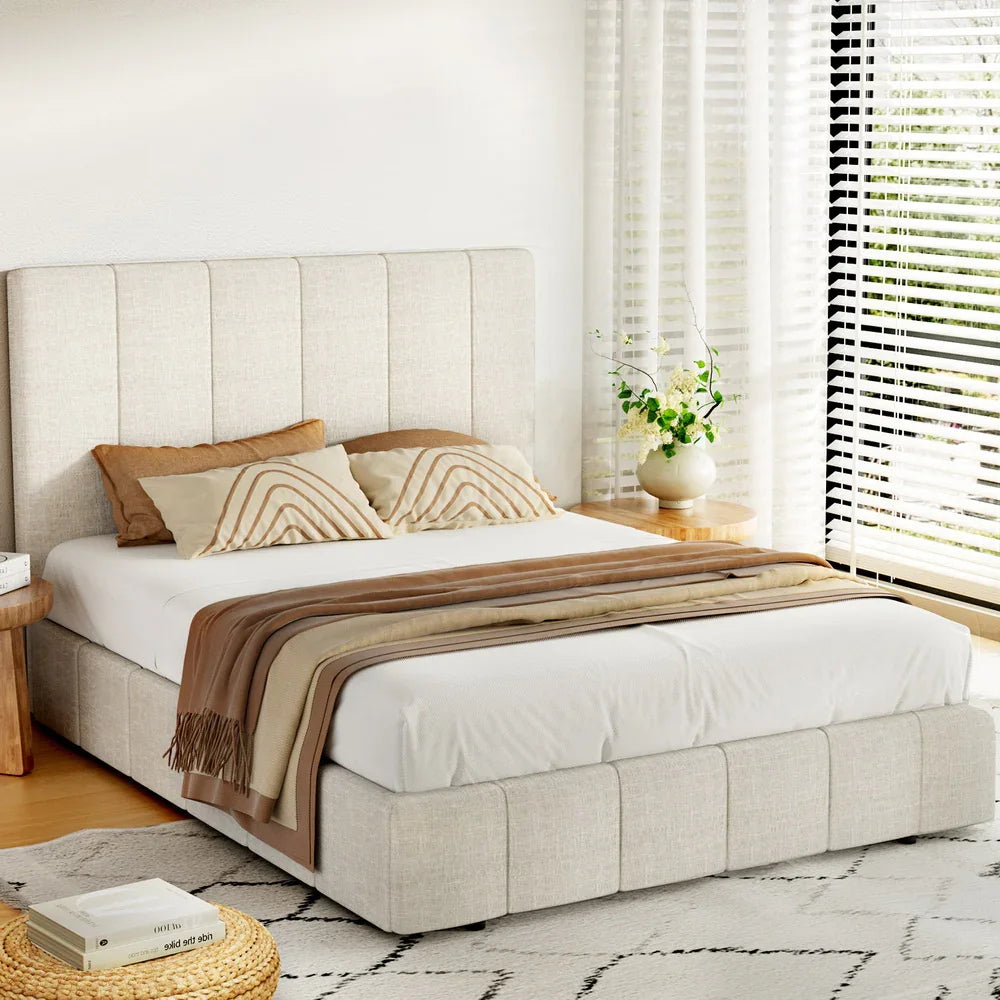 Modern bedroom with beige upholstered platform bed, patterned pillows, brown throw, and bright window blinds