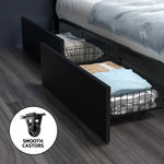 Black under-bed storage drawer with folded blankets and pillows on dark wooden floor