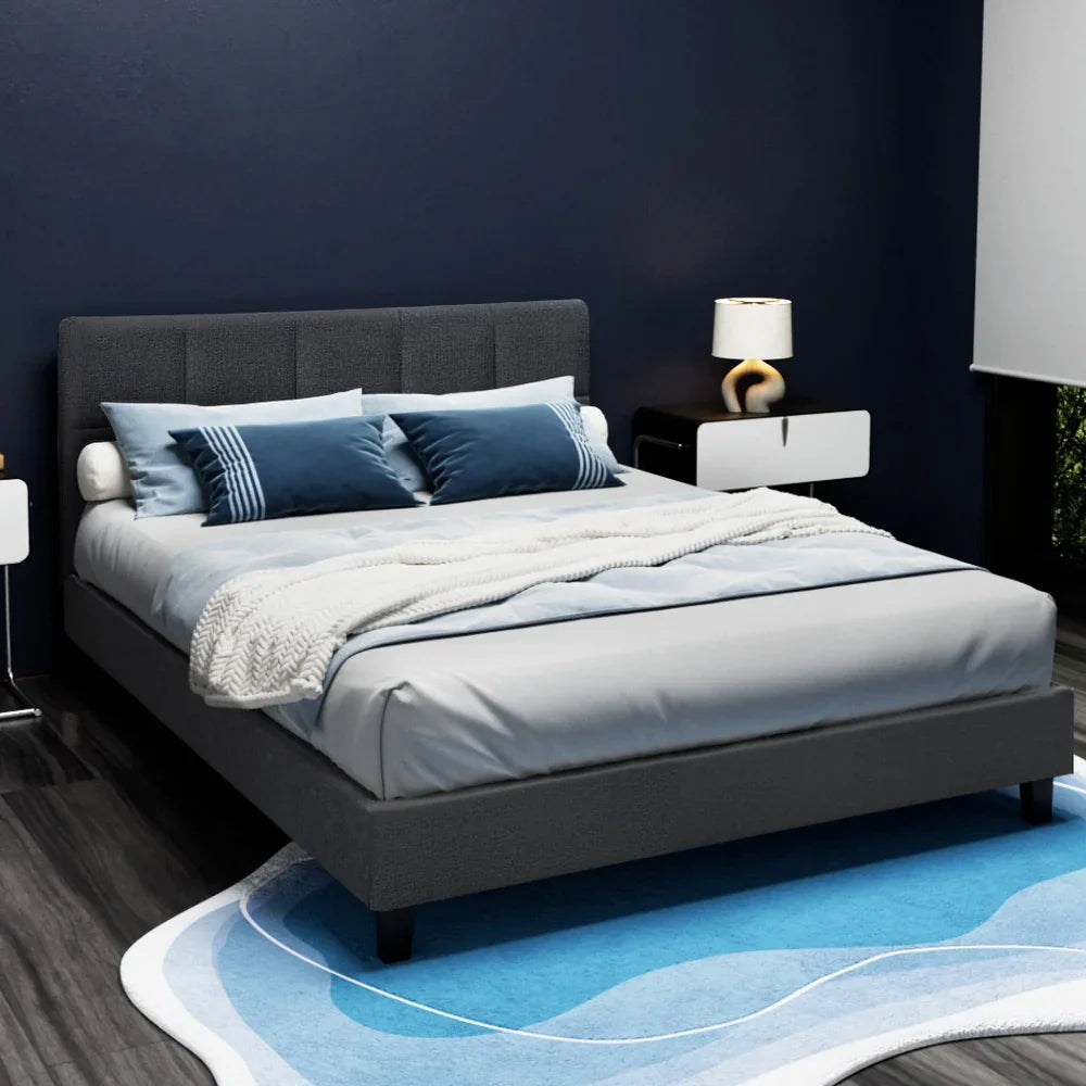 Modern bedroom with dark gray upholstered bed, blue pillows, white throw, blue abstract rug, and nightstand with lamp