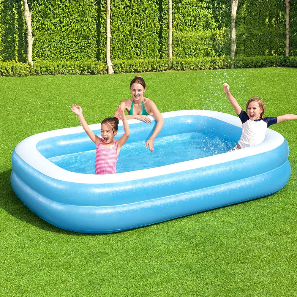 Kids and woman playing joyfully in blue inflatable pool on green grass backyard