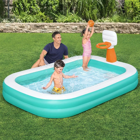 Kids playing in a turquoise inflatable pool with basketball hoop, adult watching on grass lawn