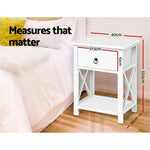 White bedside table with drawer, next to bed, measurements labeled in centimeters.