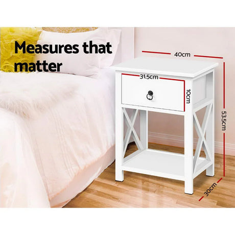 White bedside table with drawer, next to bed, measurements labeled in centimeters.