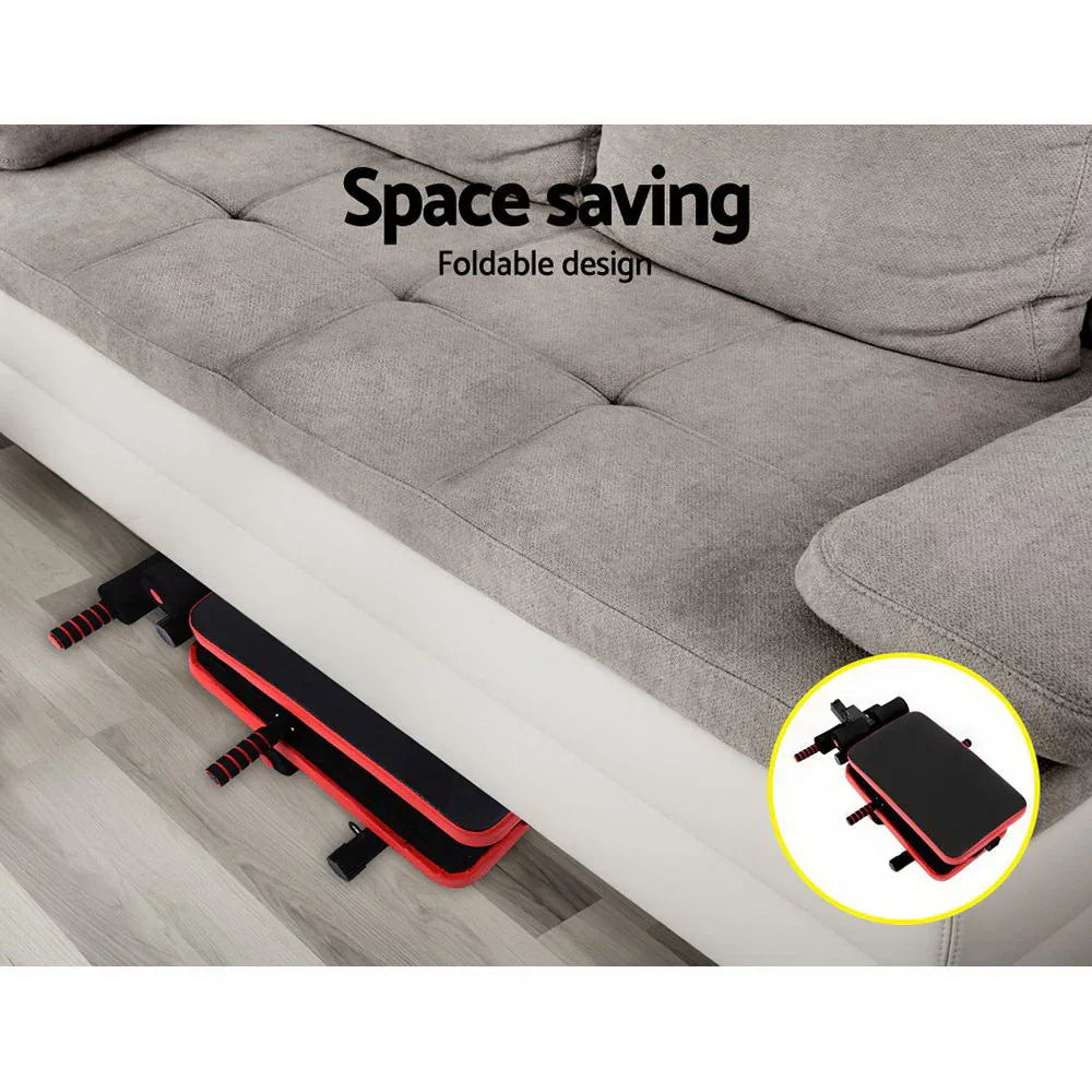 Foldable sit-up bench stored under gray sofa, space-saving home gym equipment.
