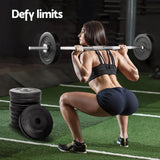 Woman performing barbell squats in gym with black weight plates stacked nearby and text Defy limits