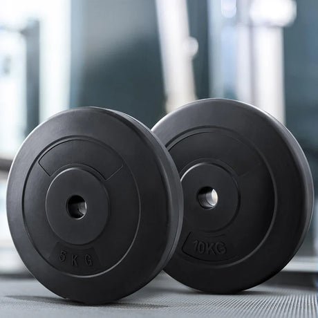 Black gym weight plates 5kg and 10kg resting on a gym floor with blurred equipment background