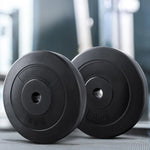 Black 5kg and 10kg rubber weight plates stacked on gym floor with blurred gym equipment background
