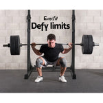 Man lifting barbell on squat rack in gym with Everfit Defy limits slogan on wall