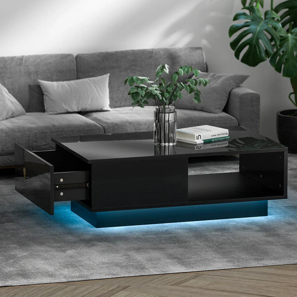 Modern black coffee table with LED lighting, glass vase, books, in a gray living room.