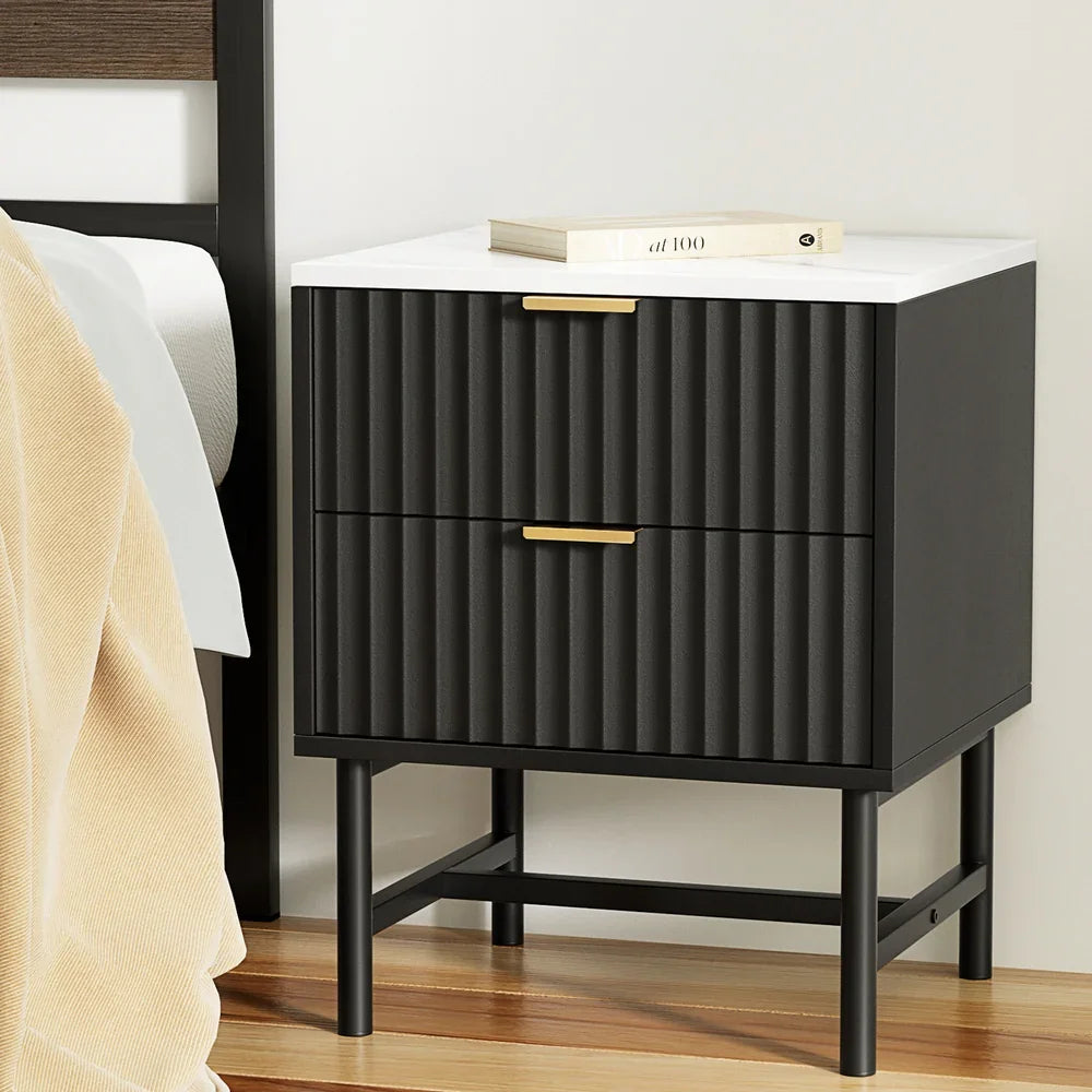 Modern black nightstand with gold handles and fluted drawers beside a bed