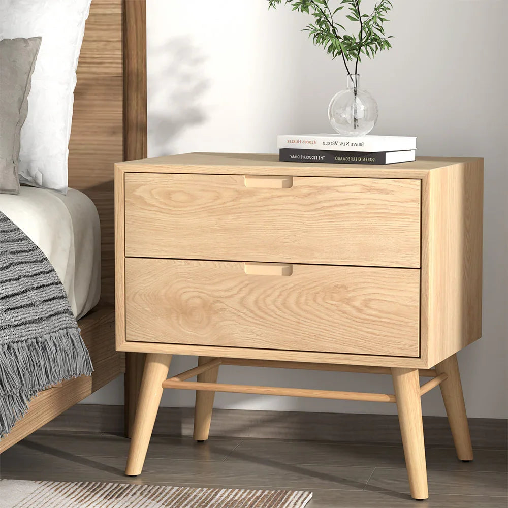 Modern light wood nightstand with two drawers beside bed, books and plant on top
