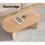 Oval wood coffee table with round edge, on grey rug, magazine and cup on top