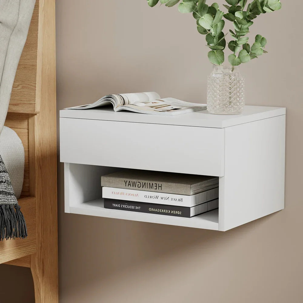 Modern white wall-mounted bedside table with books, glass vase, and greenery
