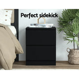 Modern black nightstand with books and decor, beside bed and plant in cozy bedroom.