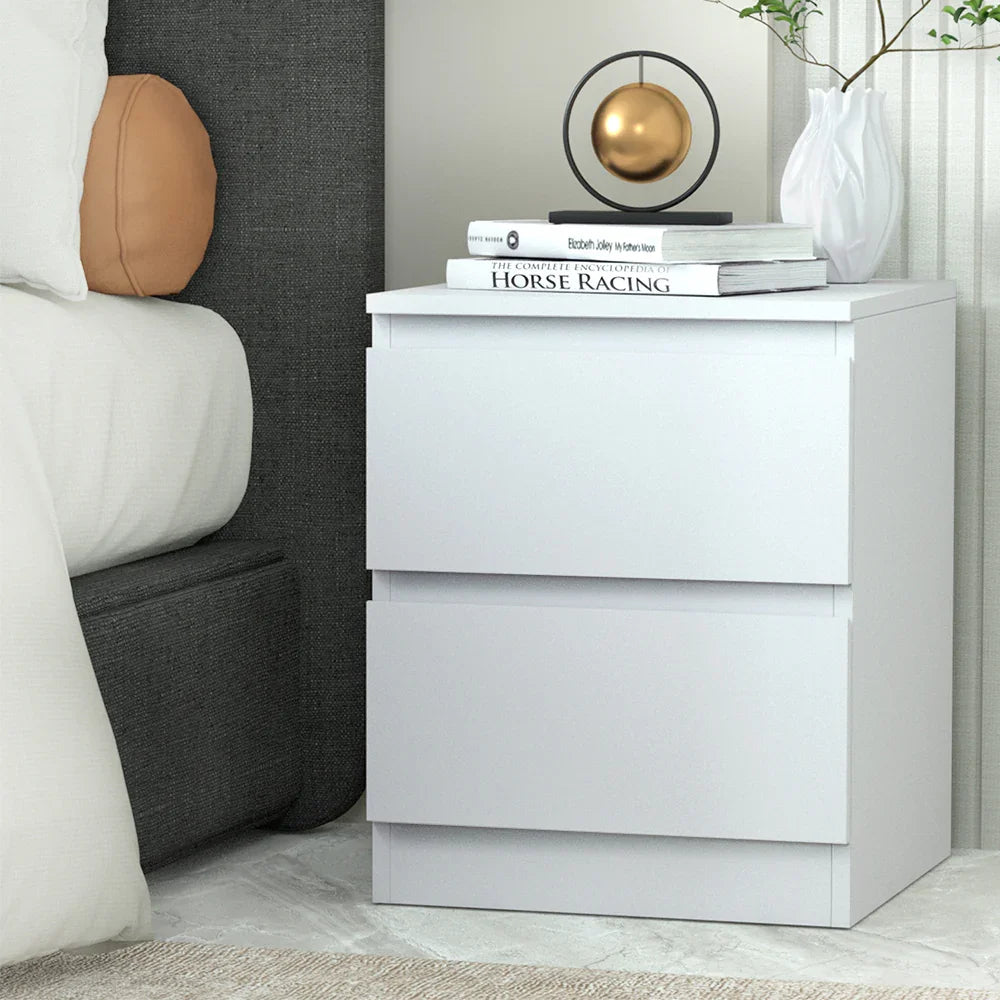 Modern white bedside table with books, decor, and vase beside a bed