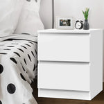 Modern white bedside table with two drawers, next to a bed with polka dot bedding