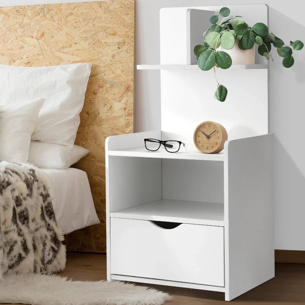 Modern white nightstand with drawer, shelf, wooden clock, glasses, potted plant by bed