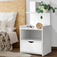 Modern white nightstand with drawer, shelf, wooden clock, glasses, potted plant by bed