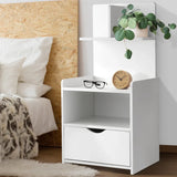 Modern white nightstand with drawer, shelf, wooden clock, glasses, potted plant by bed