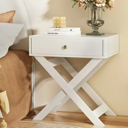 Modern white nightstand with crossed legs, decorative candle, books, and flower vase