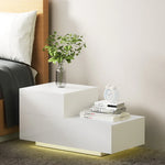 Modern white LED bedside table with books, alarm clock, and plant in a glass vase